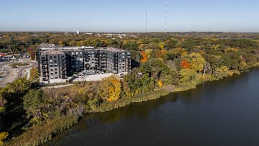 A large building sits next to a body of water with trees in the background.