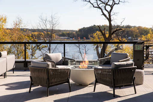 A patio with a fire pit and chairs overlooking a body of water.