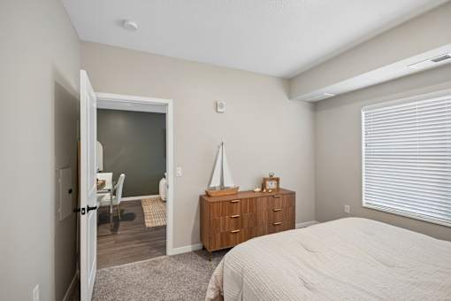 A bedroom with a bed, dresser, and a window with blinds.