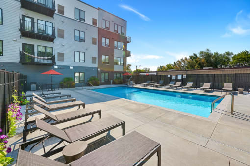 a swimming pool with lounge chairs and umbrellas in front of an apartment building at The Morrison, Rosemount, MN