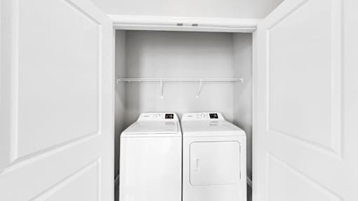 Two white washing machines in a white laundry room.