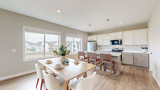 A dining room with a table set for four and a kitchen area in the background.