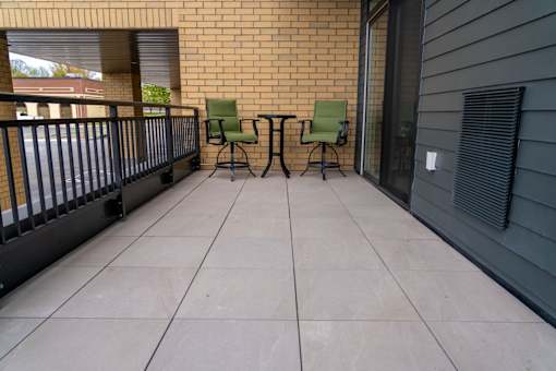 Two green chairs on a balcony with a brick wall.