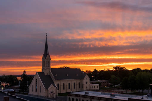 A church with a steeple is silhouetted against a sunset sky.
