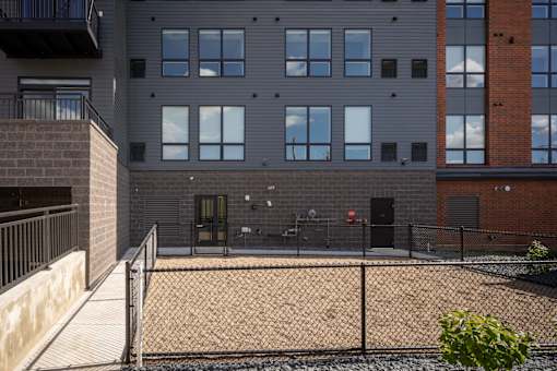 A grey building with a black fence and a red brick building to the right.