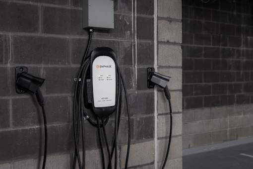 An electric vehicle charging station with a white Enphase charger plugged into a brick wall.
