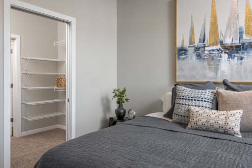 A bedroom with a grey bedspread and a painting of sailboats on the wall.