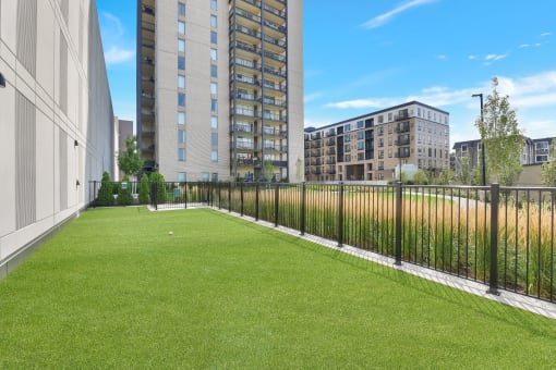 an apartment balcony with grass and a fence and buildings in the background