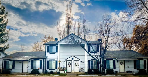 the front of a white house with blue skies and trees