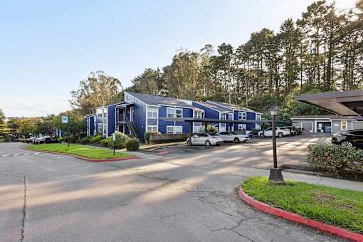 A parking lot with a blue building and a white car parked in front of it. at Skyline Heights Apartments, Daly City, 94015