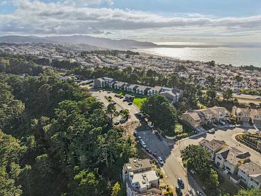 A bird's eye view of a residential area with houses surrounded by trees and a body of water in the distance. at Skyline Heights Apartments, California, 94015