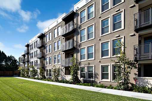 Apartment building with balconies and green lawn in front. at Cirrus Redwood City Apartments, California