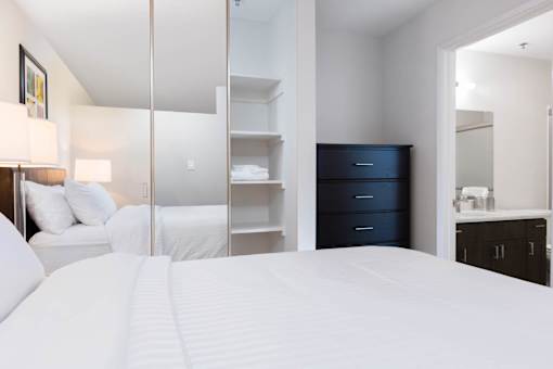 A bedroom with a large bed, a dresser, and a mirror. at The Maddox Sunnyvale Apartments, Sunnyvale, 94087