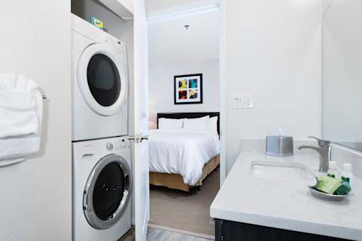 A small white bathroom with a washing machine and a bed. at The Maddox Sunnyvale Apartments, Sunnyvale