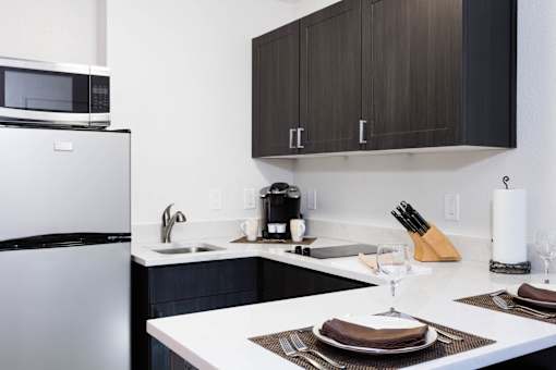 A modern kitchen with a white countertop and brown cabinets. at The Maddox Sunnyvale Apartments, California