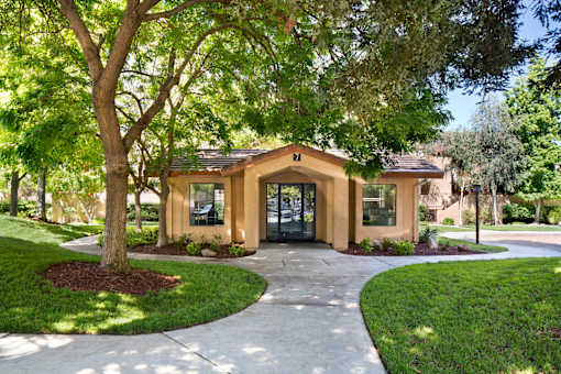 A small building with a brown roof and tan walls is surrounded by trees and grass. at The Maddox Sunnyvale Apartments, Sunnyvale, CA, 94087