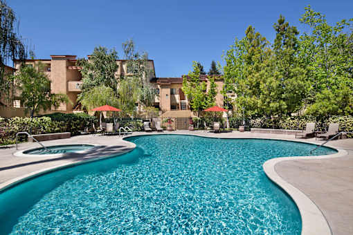 A swimming pool in front of a building surrounded by trees. at The Maddox Sunnyvale Apartments, Sunnyvale, 94087