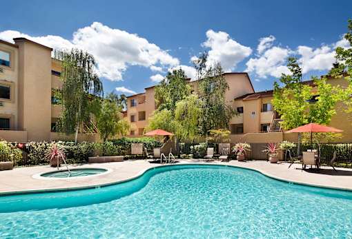 A swimming pool surrounded by chairs and umbrellas in a sunny day. at The Maddox Sunnyvale Apartments, Sunnyvale, CA, 94087