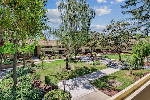 a courtyard with trees and grass and a building in the background at Summerwood Apartments, California