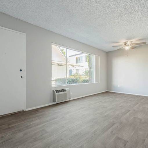 an empty living room with a large window and a ceiling fan at The Arches Apartments, California, 92021