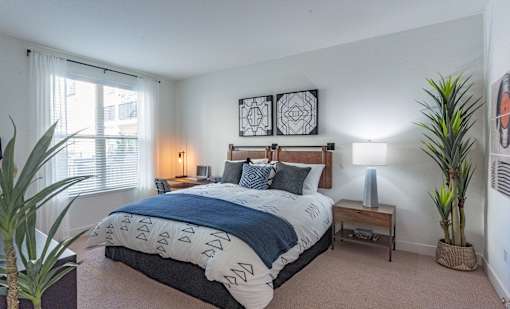 A bedroom with a large bed and two potted plants.