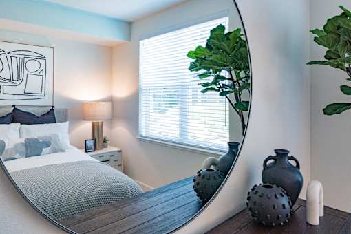 A bedroom with a round mirror and a bed with a grey blanket.