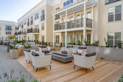 A patio with white chairs and a table with a cushion on it.