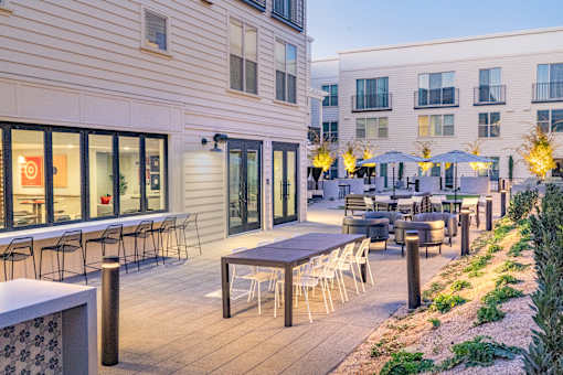 A patio with tables and chairs is surrounded by buildings.