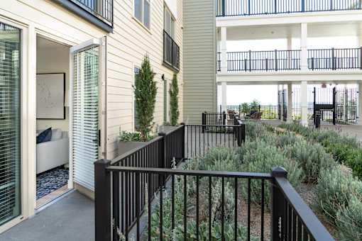 A black railing leads to a patio with a couch and a tree.