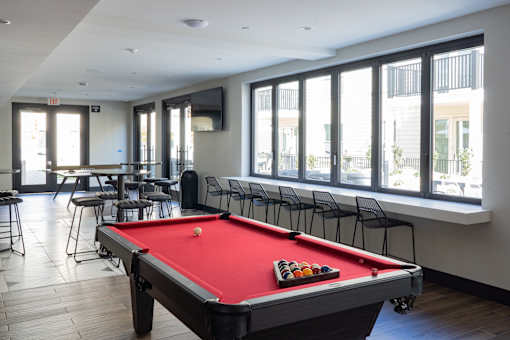 A pool table is in the middle of a room with a TV and a row of chairs.