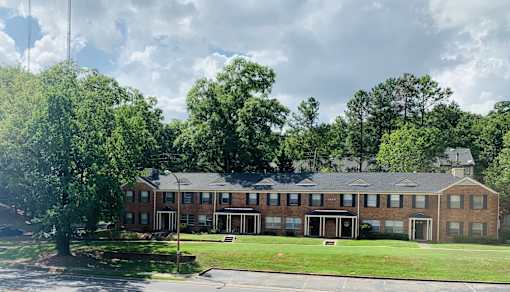 the front of a brick building with a lawn and trees
