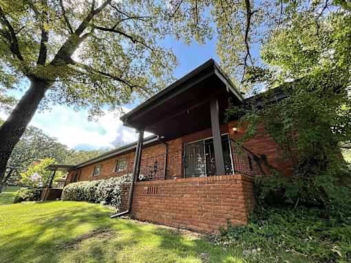 the front of a brick house with a yard and a tree