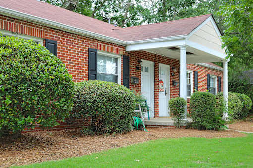 the front of a brick house with a porch and a lawn