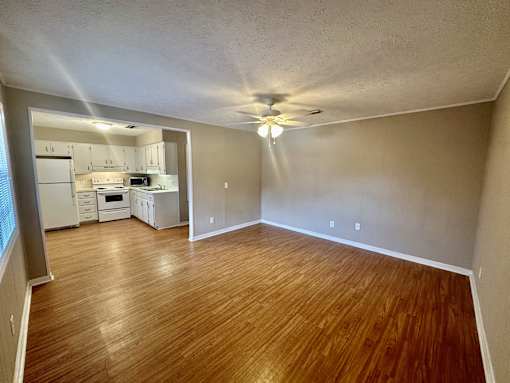 an empty living room and kitchen with wood floors and a ceiling fan