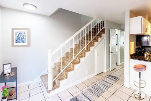 A staircase with a white railing and beige carpeted steps leads to a kitchen area.