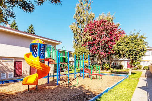 A playground with a yellow slide and a red bench.