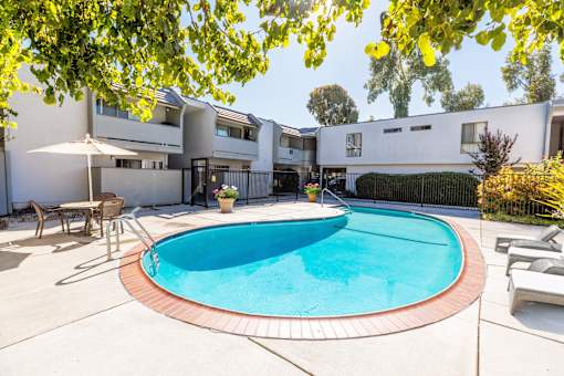 A swimming pool in a backyard with a white fence and a house in the background.