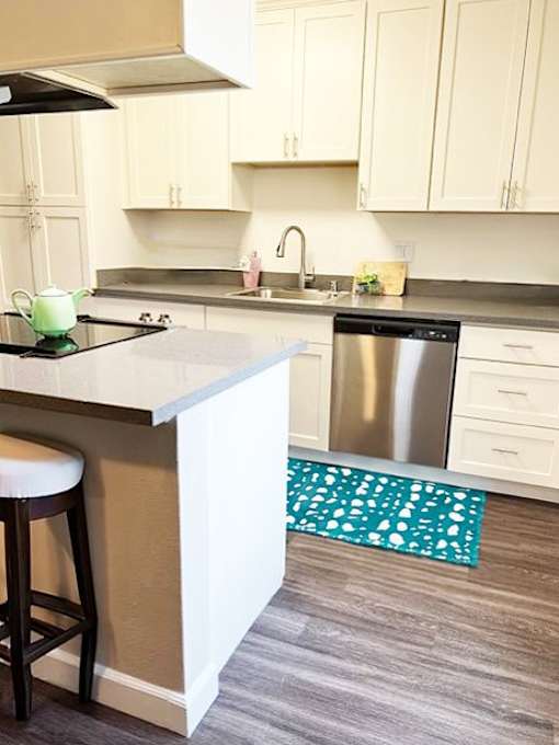 A kitchen with a stove, sink, and bar stool.