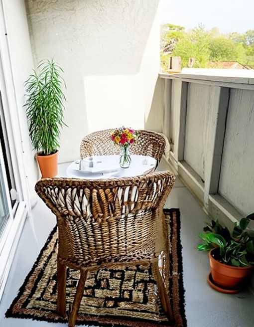 A balcony with a wicker chair and table with a potted plant on the side.