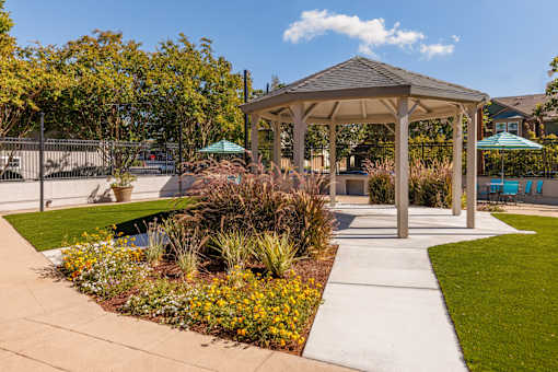 A gazebo is surrounded by a garden with a pond and a fence.