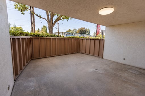 A patio with a white wall and a brown fence.