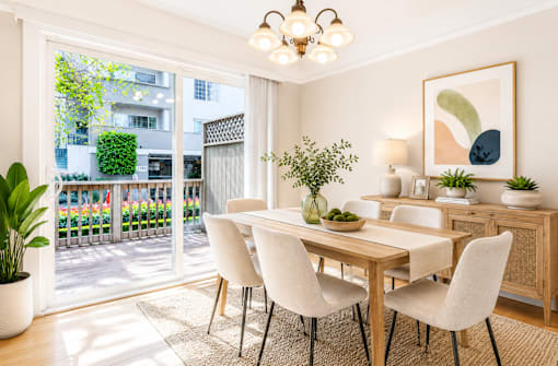 A dining room with a table and chairs and a balcony with plants.