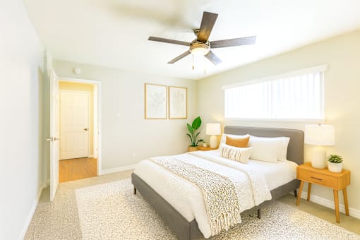 A bedroom with a bed, a ceiling fan, and a nightstand with a plant on it.