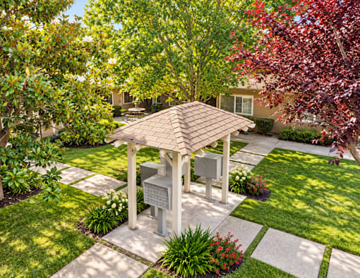 A gazebo is surrounded by a garden with a house in the background.