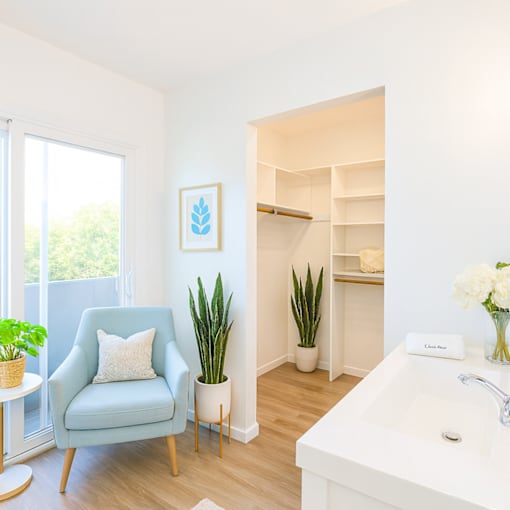 A blue chair sits in a white bathroom with a white sink and a window.