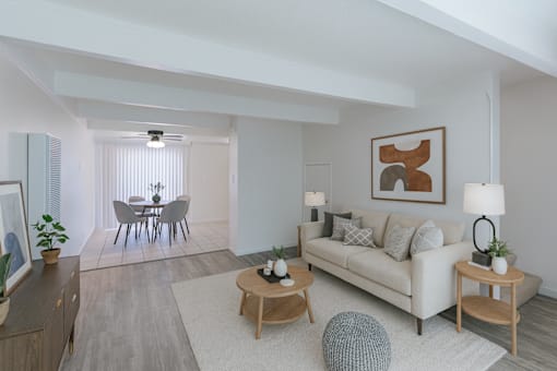 A living room with a white couch, a dining table with chairs, and a ceiling fan.