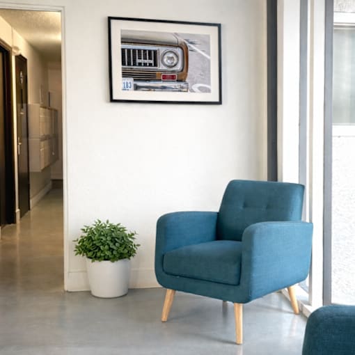 A blue chair sits in front of a framed picture of a car.