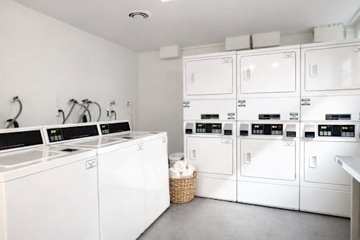 A laundry room with a washer and dryer on the left and a stack of dryers on the right.