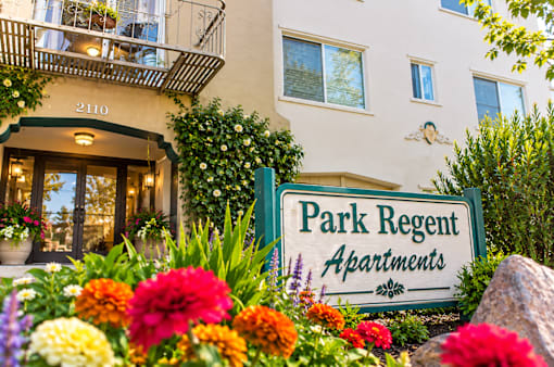 A sign for Park Regent Apartments is surrounded by flowers.