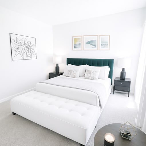 A white bed with a green headboard is in a room with a white wall and a black and white picture.